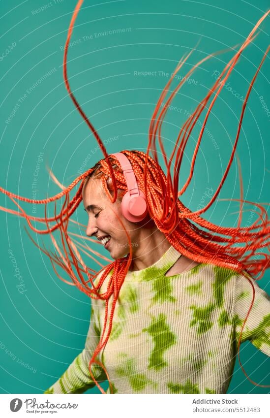 Cheerful woman with Afro braids listening to music on headphones dance vibrant portrait meloman stylish studio shot energy excited happy enjoy smile cheerful