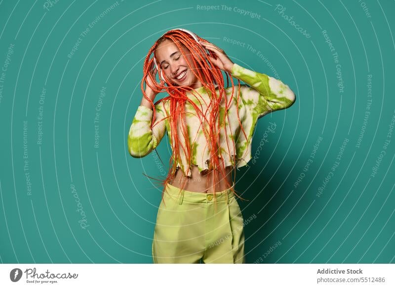 Cheerful woman with Afro braids listening to music on headphones dance vibrant portrait meloman stylish studio shot energy excited happy enjoy smile cheerful
