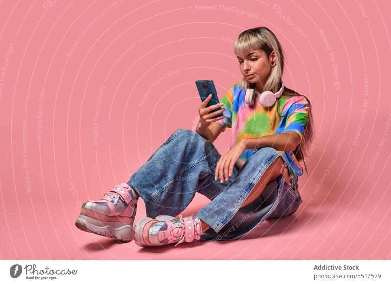 Young female hipster using smartphone in studio woman surfing internet headphones studio shot piercing message young blond trendy street style urban bangs