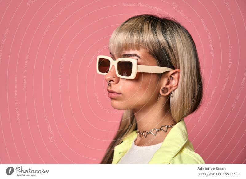Trendy female model with sunglasses woman trendy posture studio shot portrait piercing confident fashion self assured cool unemotional young style blond bangs