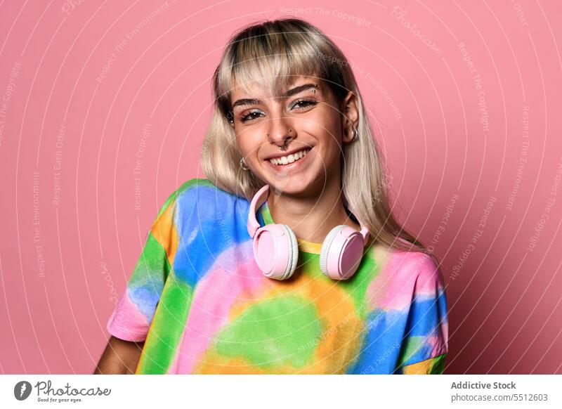 Smiling female hipster with headphones around neck woman portrait hand behind head bright model modern studio shot piercing carefree positive smile young blond