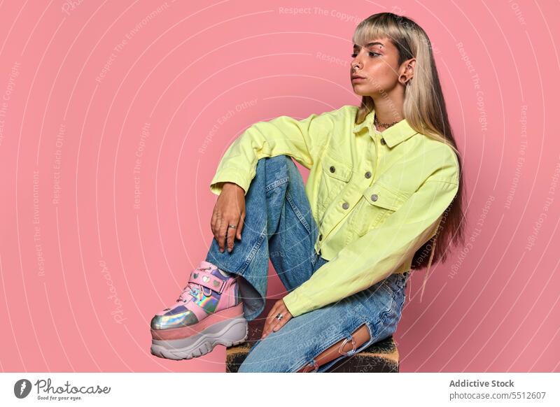 Confident young female hipster sitting on cube woman trendy posture studio shot model informal subculture piercing confident self assured unemotional cool urban