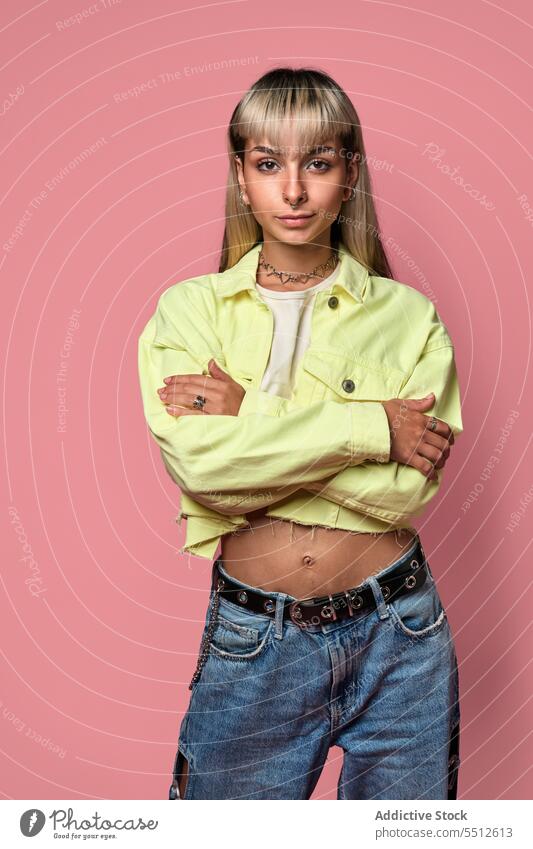 Trendy female model with arms crossed woman trendy posture portrait studio shot piercing confident fashion self assured cool unemotional young style blond bangs