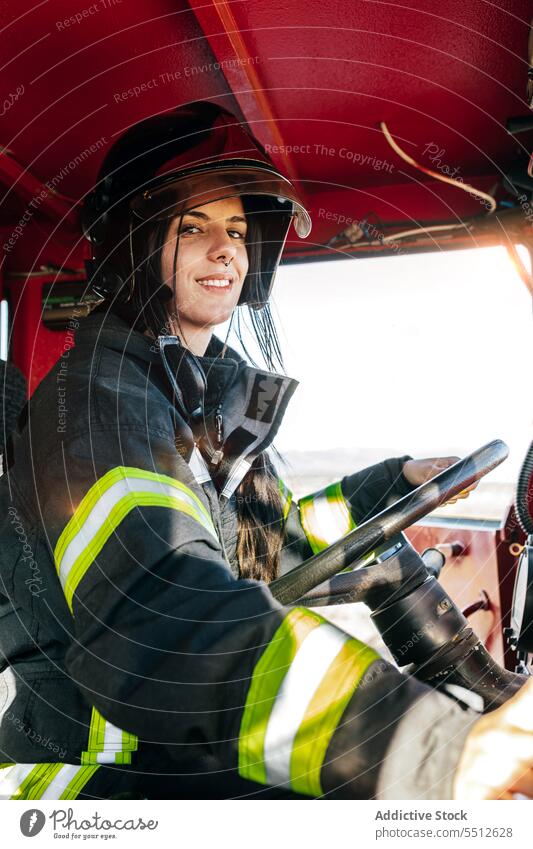 Smiling female firefighter driving fire truck woman driver fire engine vehicle service brave smile happy young firewoman black hair protect fearless transport