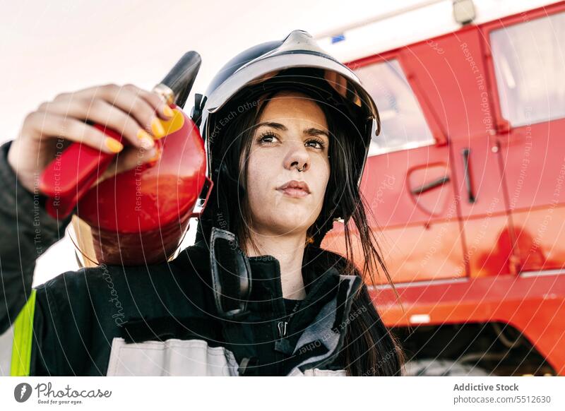 Brave female firefighter carrying fire extinguisher woman fire engine truck rescue service brave help hero serious young firewoman black hair emergency job