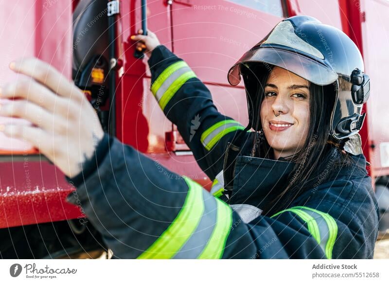 Smiling female firefighter getting into fire engine woman at work driver truck staff rescue service profession smile happy young firewoman black hair uniform