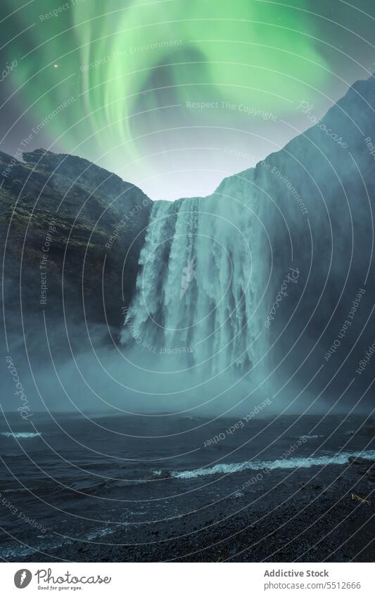 Powerful waterfall flowing through rocky slope under northern lights landscape mountain polar aurora aurora borealis phenomenon majestic iceland europe scenery