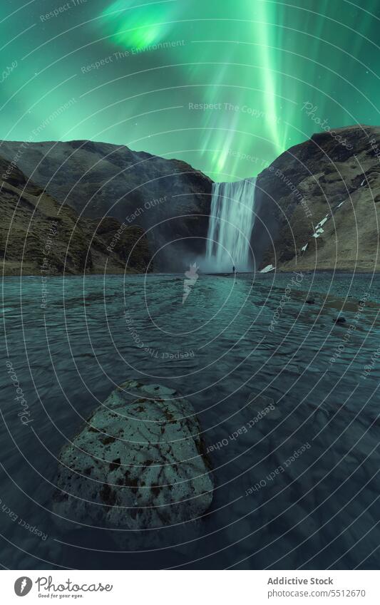 Powerful waterfall flowing through rocky slope under northern lights landscape mountain polar aurora aurora borealis phenomenon majestic iceland europe scenery