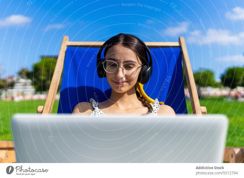 Smiling woman with laptop in headphones music listen relax summer using happy smile female enjoy device gadget chair young sound audio chill computer eyeglasses