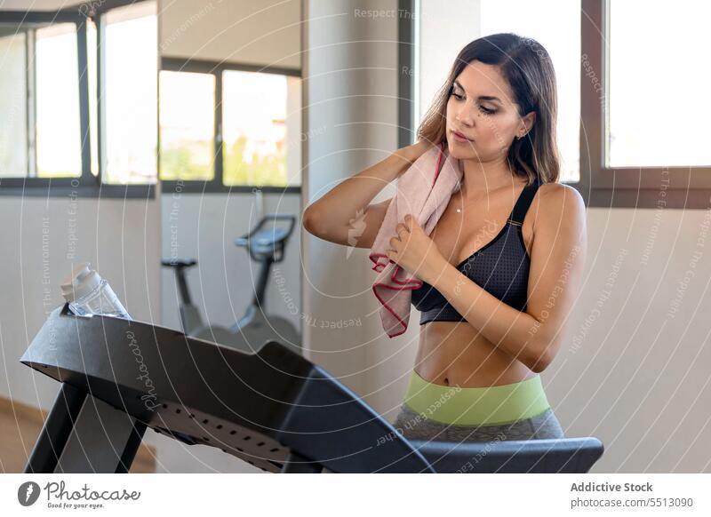 Young woman standing on treadmill with a towel round his shoulder tired workout exercise sweat wipe training fit gym female young sportswear break fitness