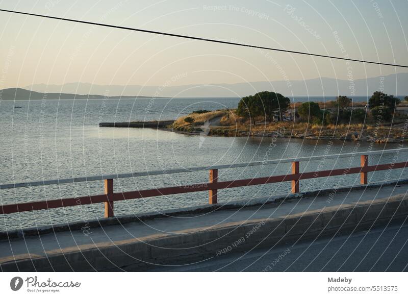 View from a bridge with railing to the sea in the light of the evening sun with coastal landscape, bay and peninsula in Cunda near Ayvalik at the Aegean Sea in Balikesir province in Turkey