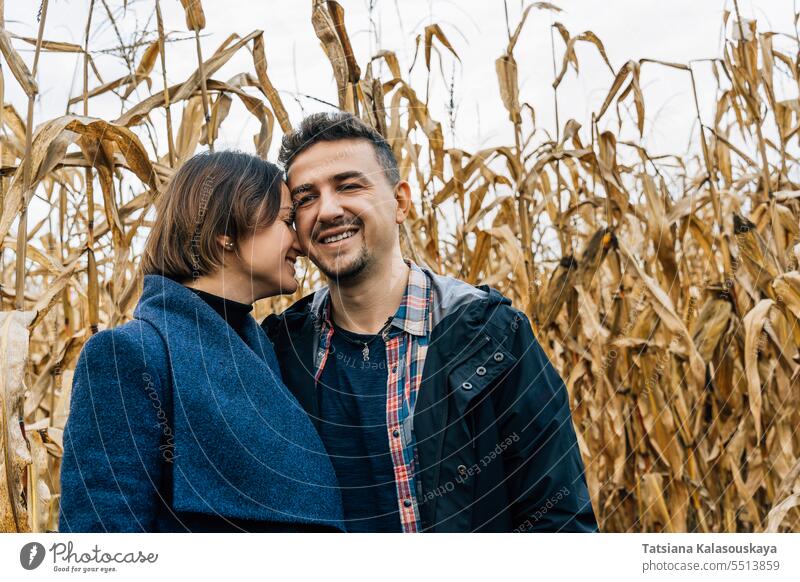 A frank moment of tenderness during a couple's walk in a cornfield in the fall. A woman presses her forehead against the cheek of her lover happy smiling