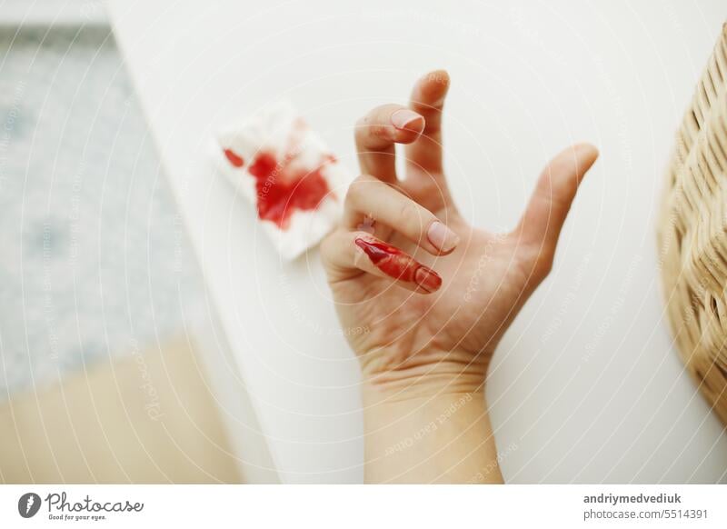 Female hand and napkin with red blood. Woman injured her little finger at home with knife or another sharp object. Domestic accident. Bleeding wound and body injury result.