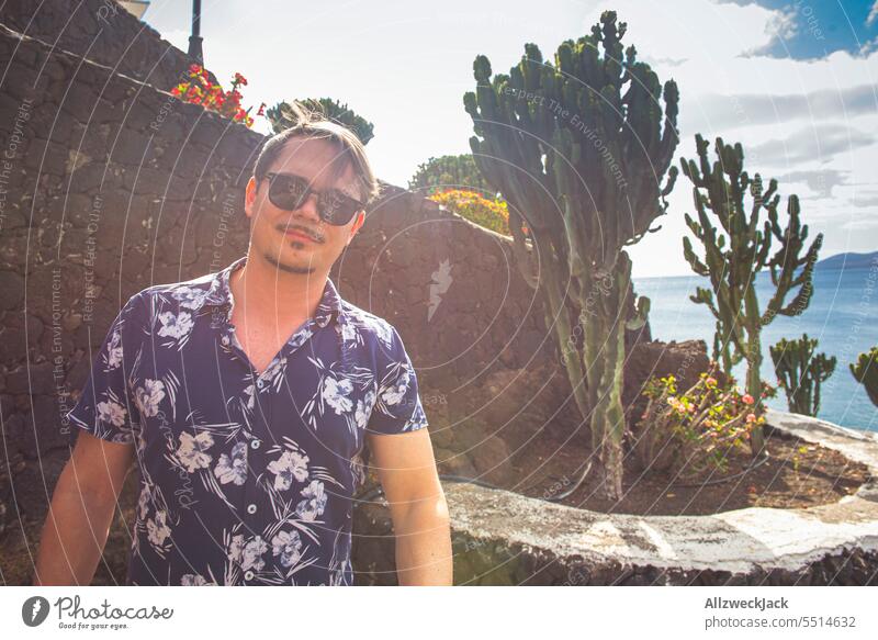 Portrait of a middle-aged man with sunglasses in front of a stone wall and next to a cactus plant Man portrait Short sleeve short-sleeved vacation Vacation mood