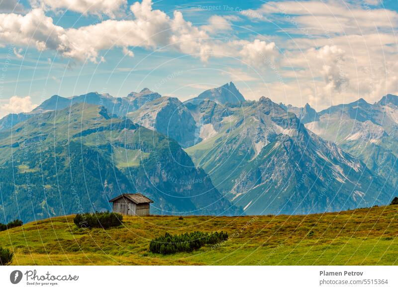 The picturesque Stubai Alps in summer, a panoramic view of peaks on the border between Austria and Italy, a wooden hay barn perched on green meadow high up above Gschnitztal valley, Tyrol, Austria.
