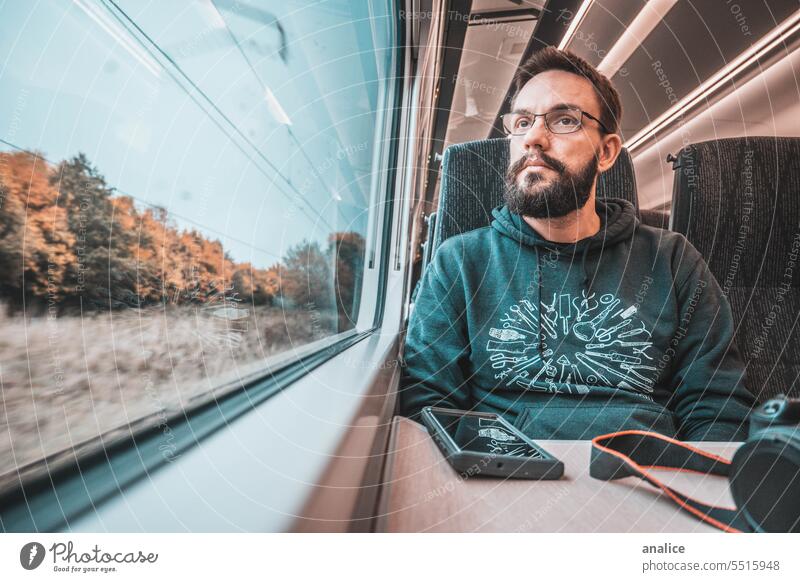 Man traveling solo by train looking outside the window male Beard bearded glasses Eyeglasses Camera Mobile Cellphone traveler looking out of window Sadness sad