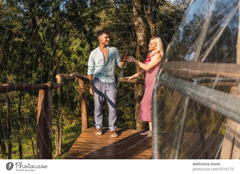 Couple with beer bottles on terrace of glamping dome couple clink vacation leisure weekend relax celebrate together summer cheers drink toast alcohol