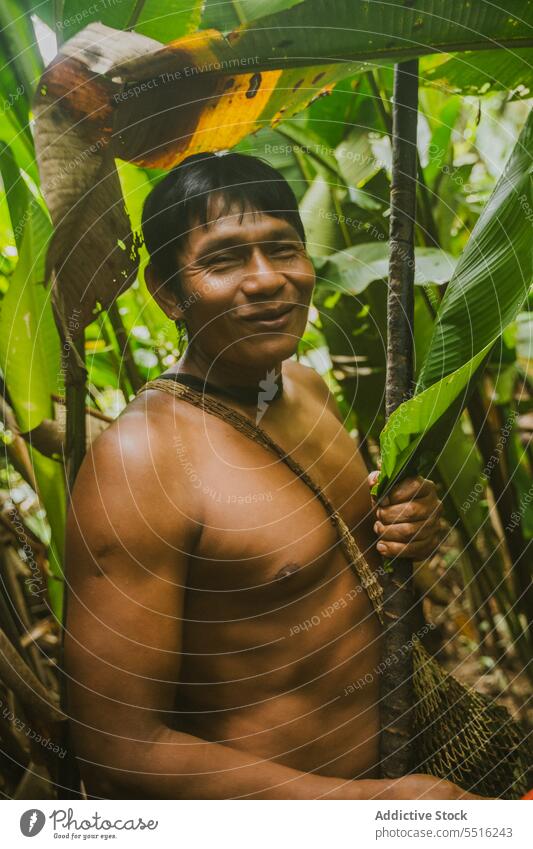 Cheerful ethnic man with stick in tropical forest jungle positive nature naked exotic cheerful male smile summer tree foliage joy happy naked torso plant