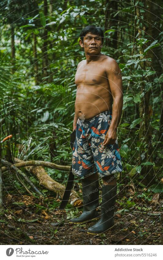 Shirtless tribal man standing in rainforest jungle tropical nature bush shirtless greenery local wood exotic ground job machete climate knife serious