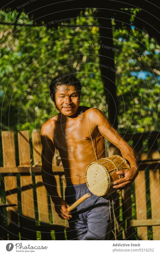 Local man playing drum in sunlight tribe village local indigenous rural walk native authentic nature tropical tradition naked torso exotic culture