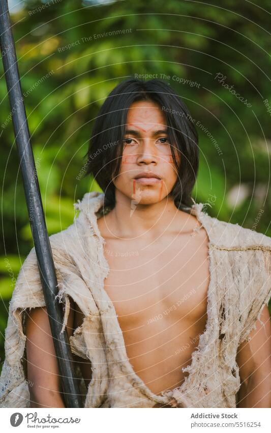 Tribal man with stick in tropical forest nature serious plant green woods exotic male ethnic young tree flora environment natural foliage summer greenery growth