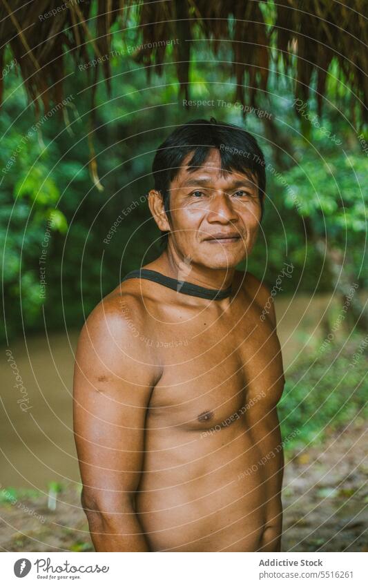 Tribal man standing in tropical forest near river stick nature plant green naked torso woods exotic male ethnic young tree flora environment natural foliage