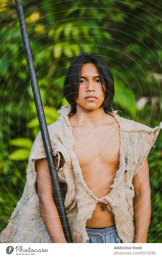 Tribal man with stick in tropical forest nature serious plant green woods exotic male ethnic young tree flora environment natural foliage summer greenery growth