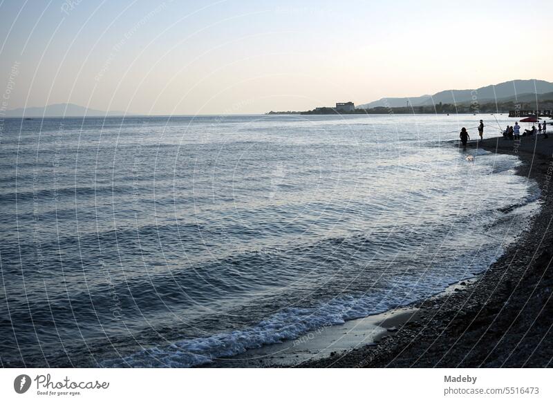 View from the beach in Altinoluk with angler in the romantic light of the setting sun on the Gulf of Edremit on the Aegean Sea in the province of Balikesir in Turkey