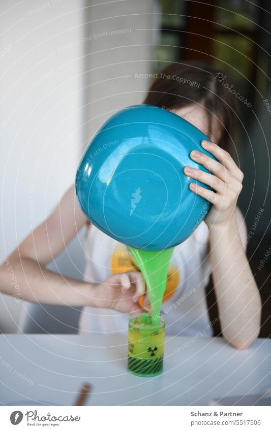 Child pours green slime from a blue bowl into a cup with radioactive warning label Playing Schleimi slimy disgusting Toys