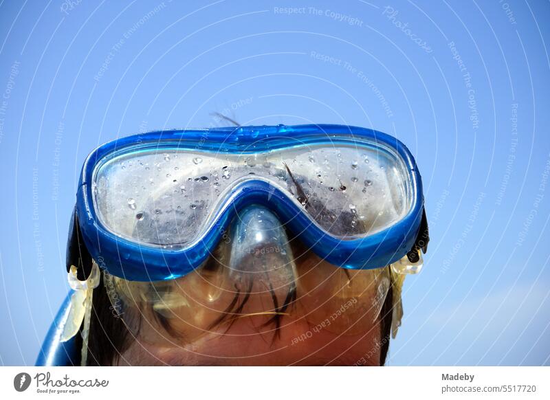 Boy with blue diving goggles and snorkel in front of blue sky in the sunshine on the beach of Sarimsakli near Ayvalik on the Aegean Sea in Balikesir province, Turkey