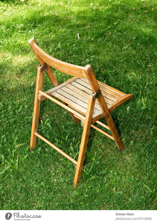 Folding wooden chair stands on a meadow Folding chair Meadow lawn seat Grass colour contrast Deserted Garden Chair Seating Break out Offside stand apart