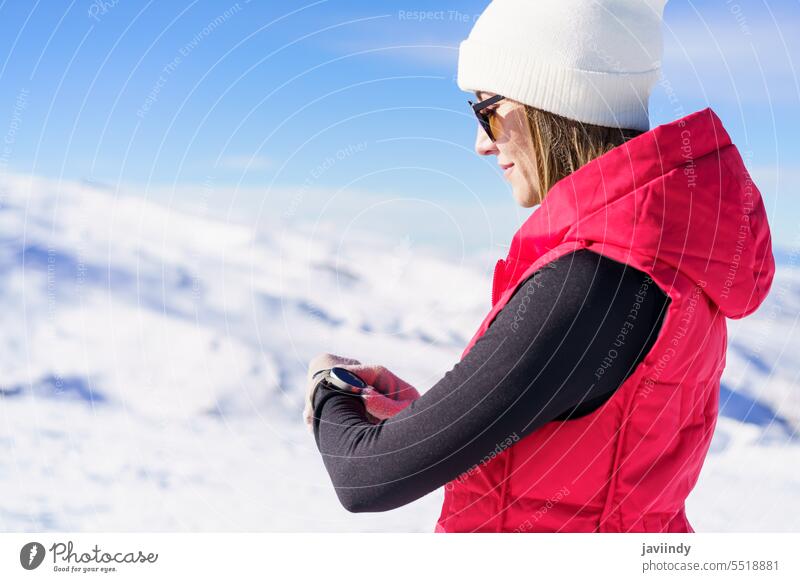 Young woman standing in snowy terrain checking time Woman Winter Wristwatch test Time Slope Adventure warm clothing Snow Mountain youthful daylight voyage