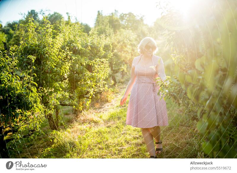 blonde middle aged woman with pink dress in orchard among pear trees Woman Middle aged woman pretty Sympathy Congenial Dress Pink Sunlight Sunbeam Summer