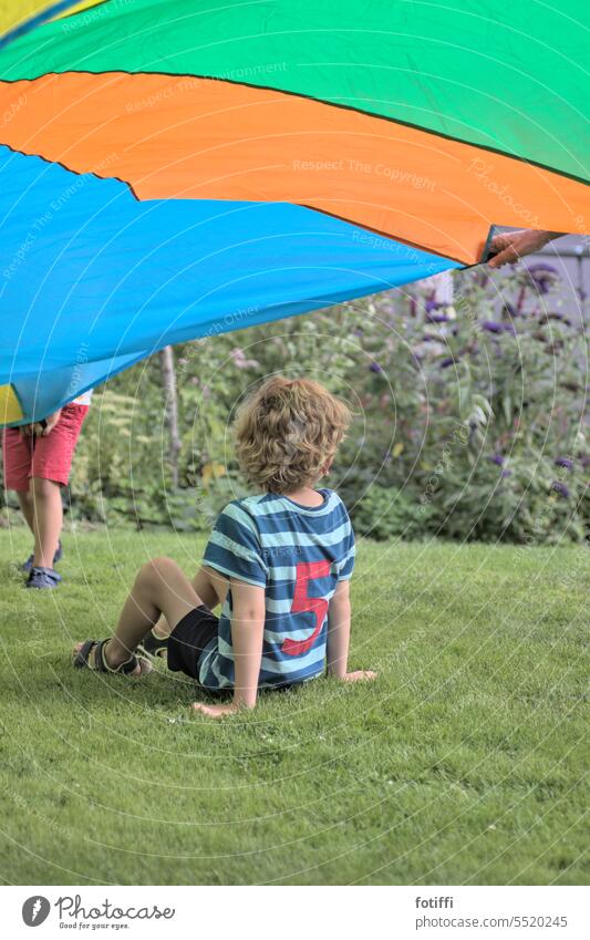 Curly-haired child sits on grass under flying swinging cloth Playing Lawn Spring Swing swing sheet absent Nature Garden Summer Grass Green Meadow Joy Flying