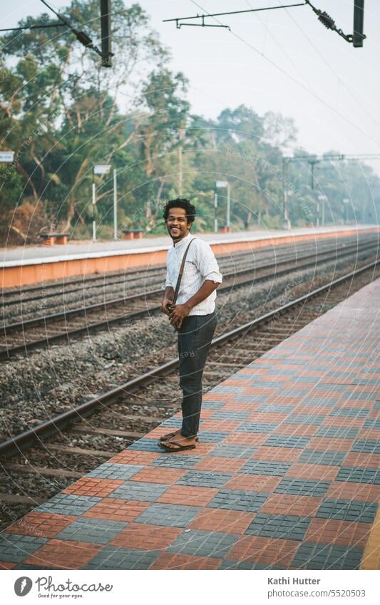 a young man is standing on the railroad track waiting for the train. A laugh is on his face Man Train station Platform Wait Transport Railroad Vacation & Travel