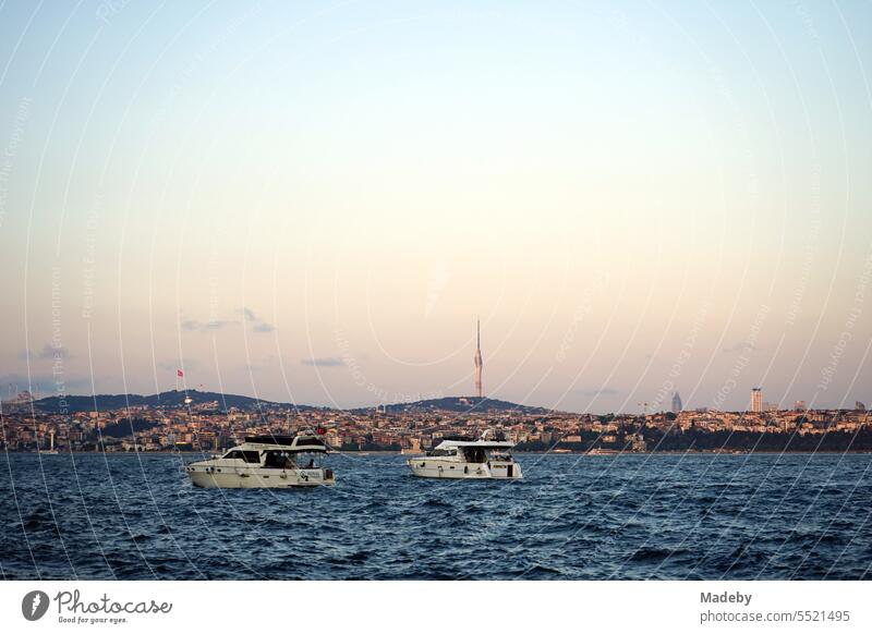 Motorboats and yachts in front of the pier of the ferry across the Bosphorus in Karaköy in the light of the setting sun with a view of the TV tower Küçük Çamlıcaim in Istanbul, Turkey