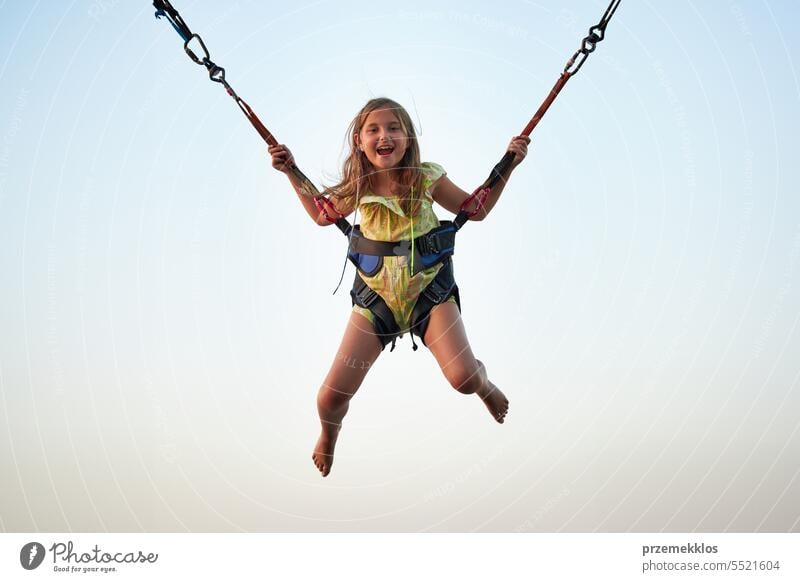 Bungee jumping at trampoline. Little girl bouncing on bungee jumping in amusement park on summer vacations playing person child fun activity sky outdoor joy