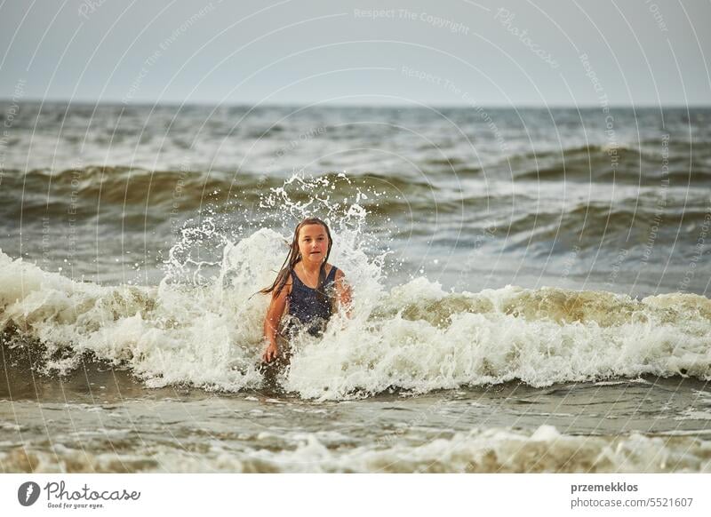 Little girl playing with waves in the sea. Kid playfully splashing in waves. Child jumping in sea. Vacations on the beach. Water splashes summer vacations ocean