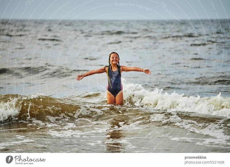 Little girl playing with waves in the sea. Kid playfully splashing in waves. Child jumping in sea. Vacations on the beach. Water splashes summer vacations ocean