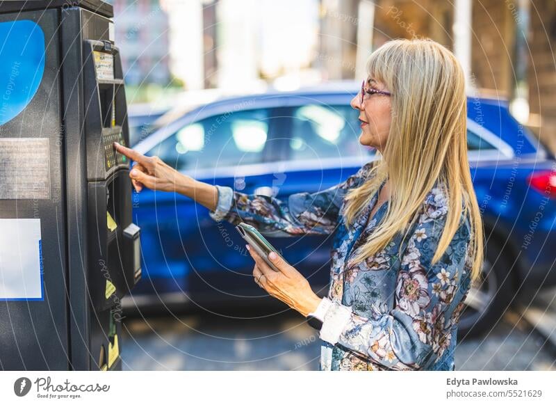 Mature woman using a mobile phone to pay for parking in the city natural enjoy satisfied cheerful confident pensioner outdoors outside eyeglasses elderly