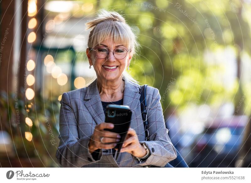 Portrait of smiling senior woman with mobile phone in the street natural enjoy satisfied cheerful confident pensioner outdoors outside eyeglasses elderly