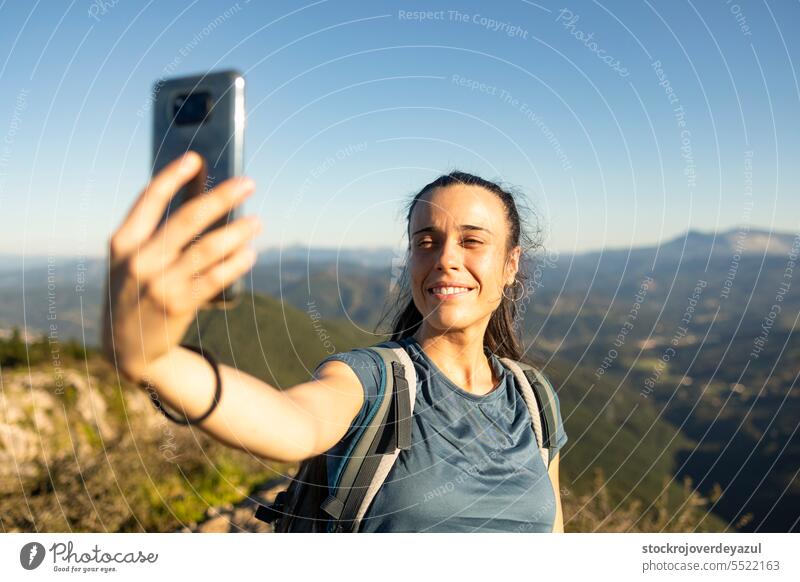 A young, happy woman smiles as she takes a selfie with her smartphone from the top of a mountain women person lifestyle female beauty mobile outdoors attractive