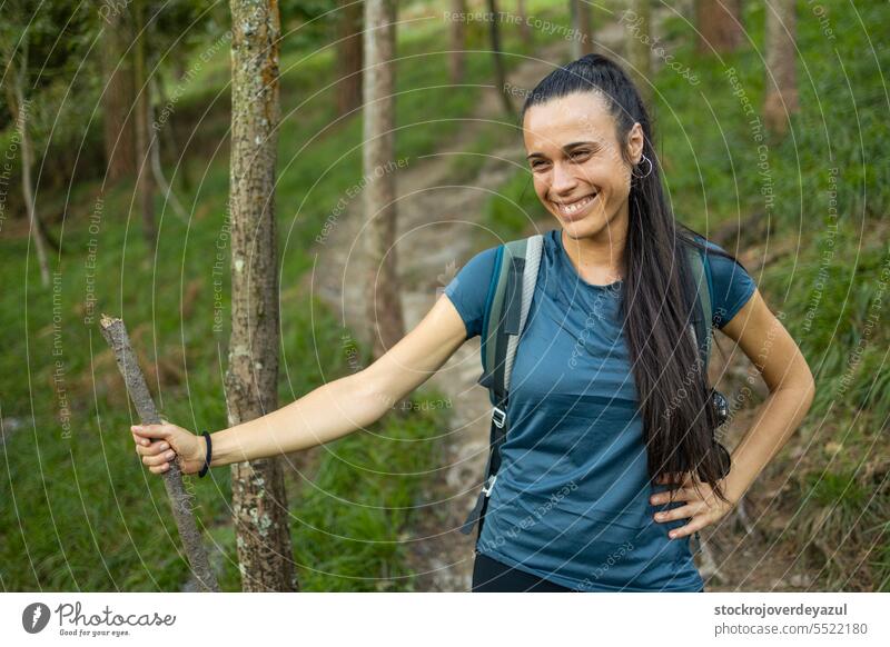 A young woman hiker with a wooden stick as a walking stick smiles and enjoys a stop during a nature walk female person lifestyle happiness portrait adult beauty