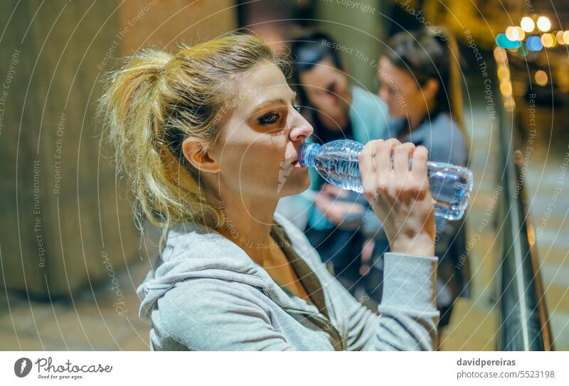 Portrait of tired woman runner drinking water after training with her friends at night on town. portrait thirsty exercise running liquid hydration sport women