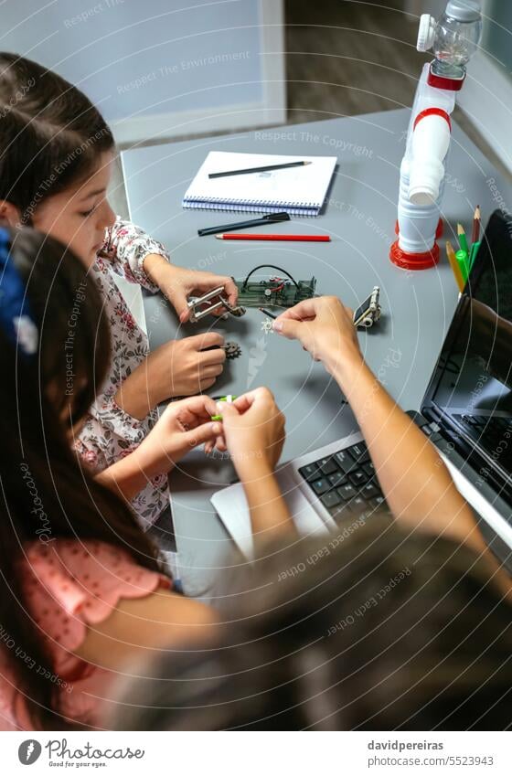 Female teacher helping girl students to assemble pieces of machine in a robotics class female unrecognizable explaining children electronic circuit electrical