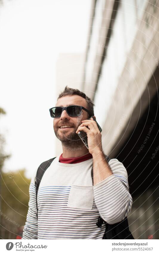 A young, traveling man wearing sunglasses, talking on a smartphone phone, on the street, in a city in Spain. male mobile men adult happy caucasian person