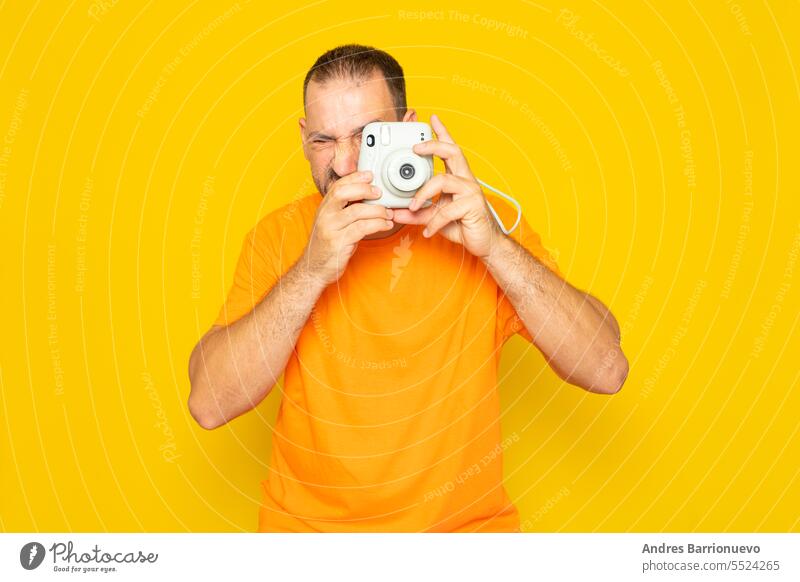Bearded Hispanic man in his 40s taking a photo with an instant camera, isolated on yellow background. lifestyle people device male mature men short hair