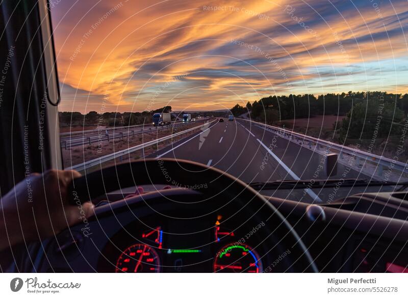 View from the driver's seat of a truck of a highway with vehicles in both directions under a dramatic sky. hand inside cabin sunset dashboard steering wheel