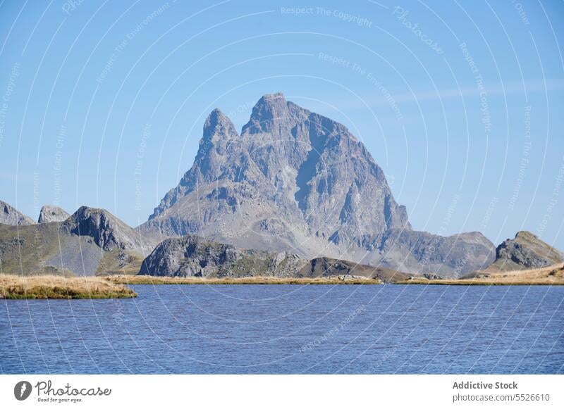Calm lake surrounded by Pic du Midi d'Ossau mountain pyrenees peak ridge stone rock slope range rocky rough scenic landscape environment meadow lawn hill french