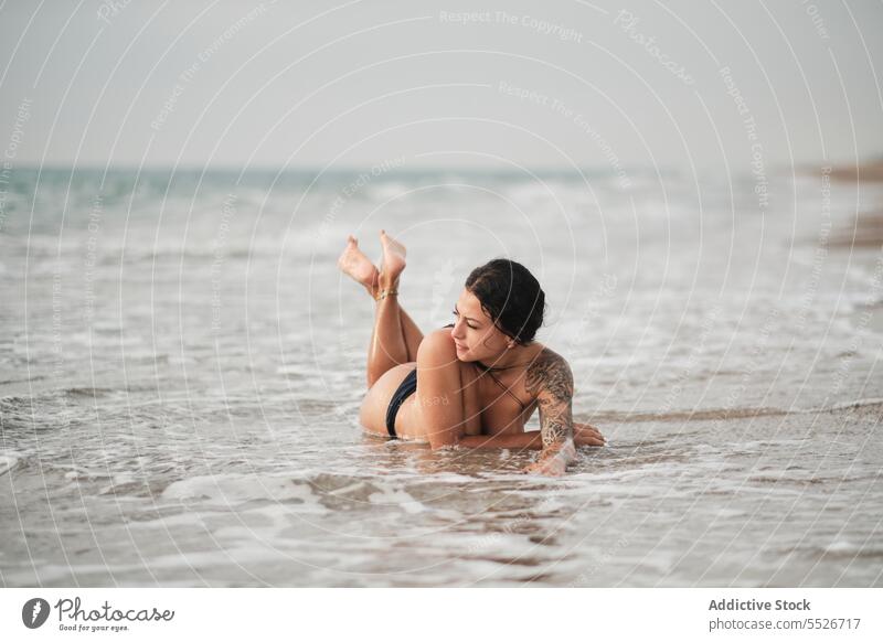 Sensual woman in bikini lying on seashore bottom topless beach enjoy foam happy relax vacation ocean female summer young pleasure coast rest swimwear carefree